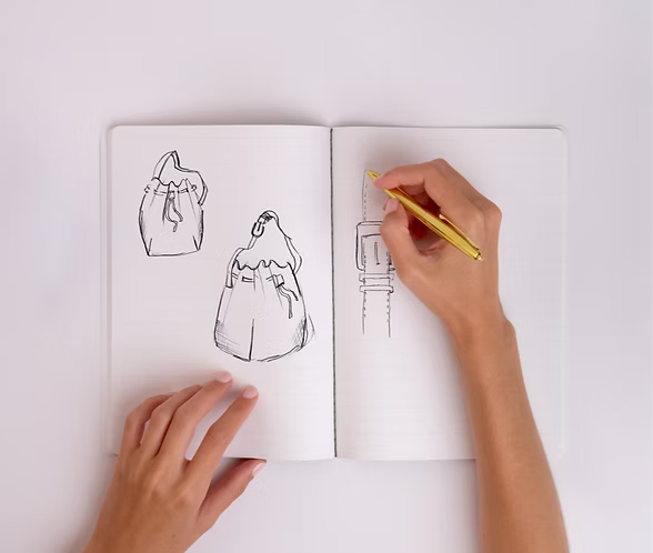 Hand sketching custom bag designs in a notebook at the concept stage of a new brand